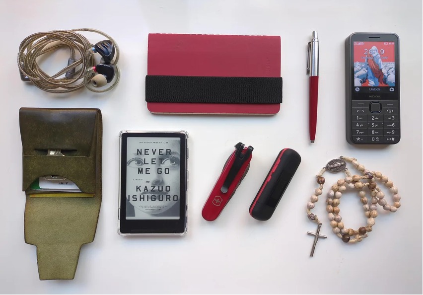 Everyday carry layout shared to r/dumbphones — earphones, notebook, pen, Nokia phone, rosary beads.