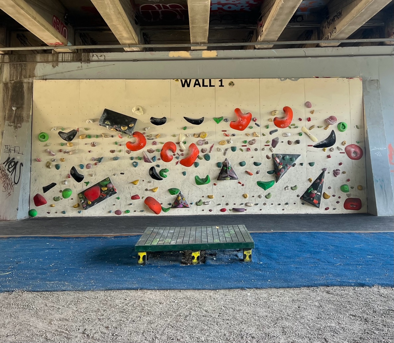 An outdoor bouldering wall beneath a bridge overpass.