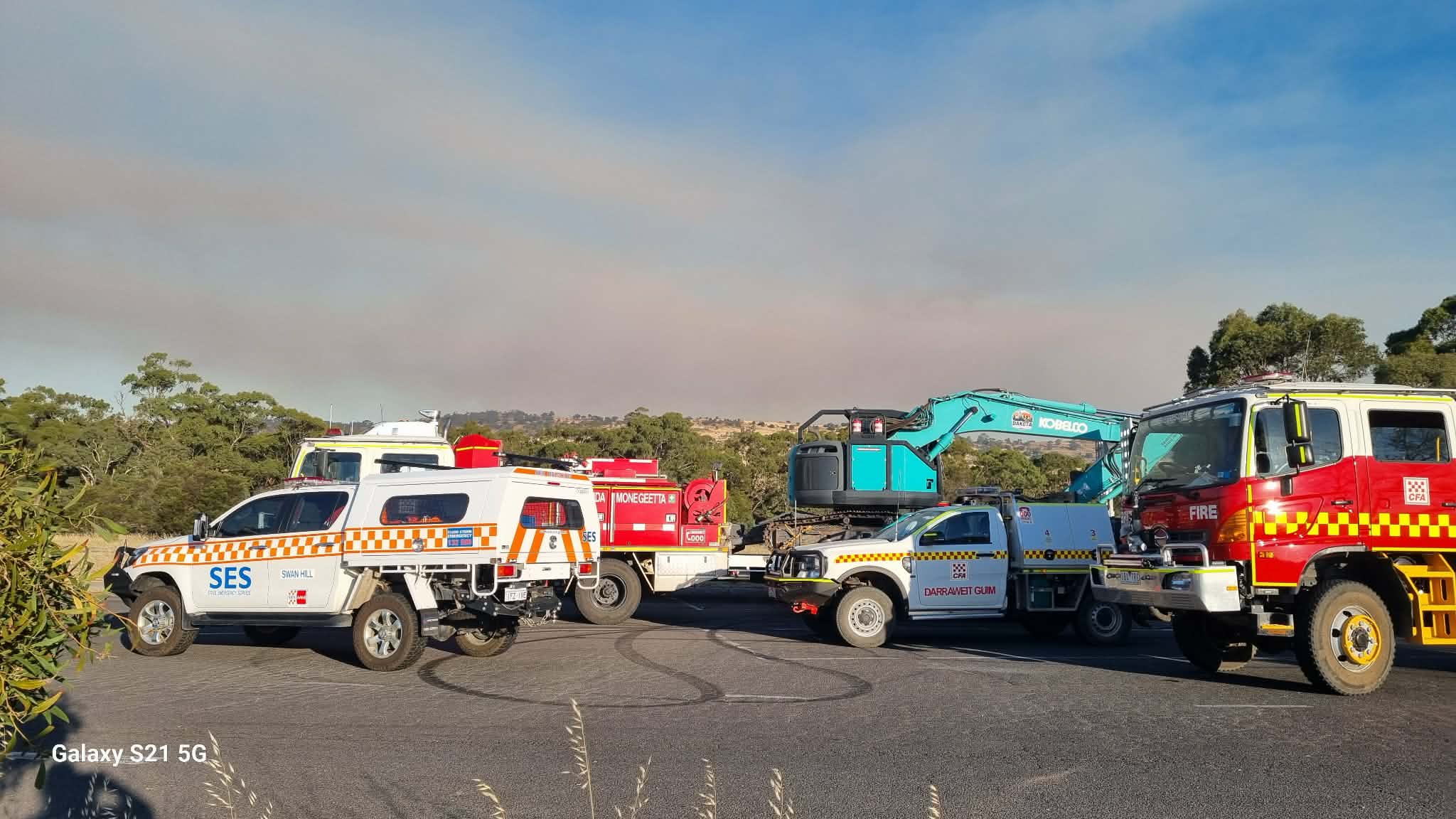 Emergency vehicle convoy staged with smoke haze in the background.